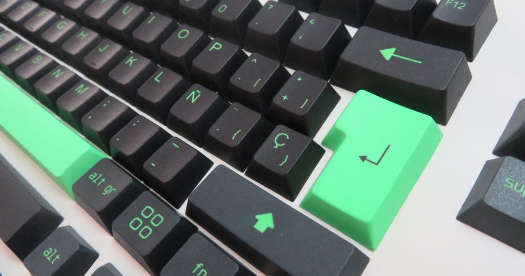 Set de keycaps en colores negro, gris y verde sobre una mesa blanca