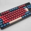 Teclas PBT uniformes y redondeadas en colores rojo,azul y beige sobre un teclado negro ISO-TKL SUN GLOW.